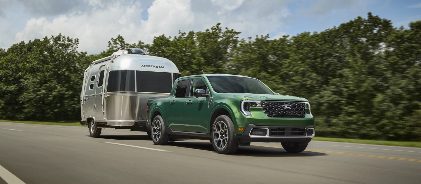 Une camionnette Ford Maverick® 2025 tirant une remorque de voyage Airstream le long d’une autoroute, avec une forêt derrière