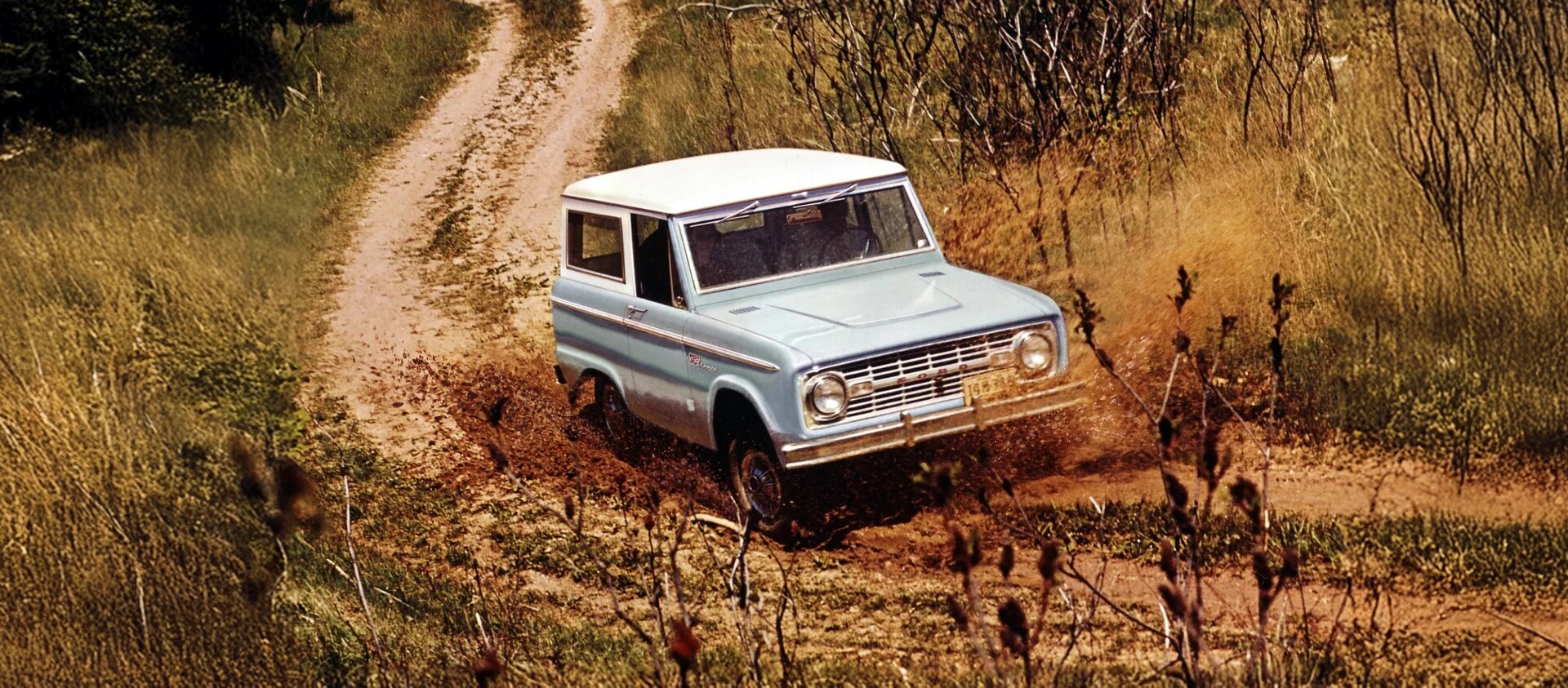 Une fourgonnette Bronco des années 1960 roulant sur un chemin de terre.