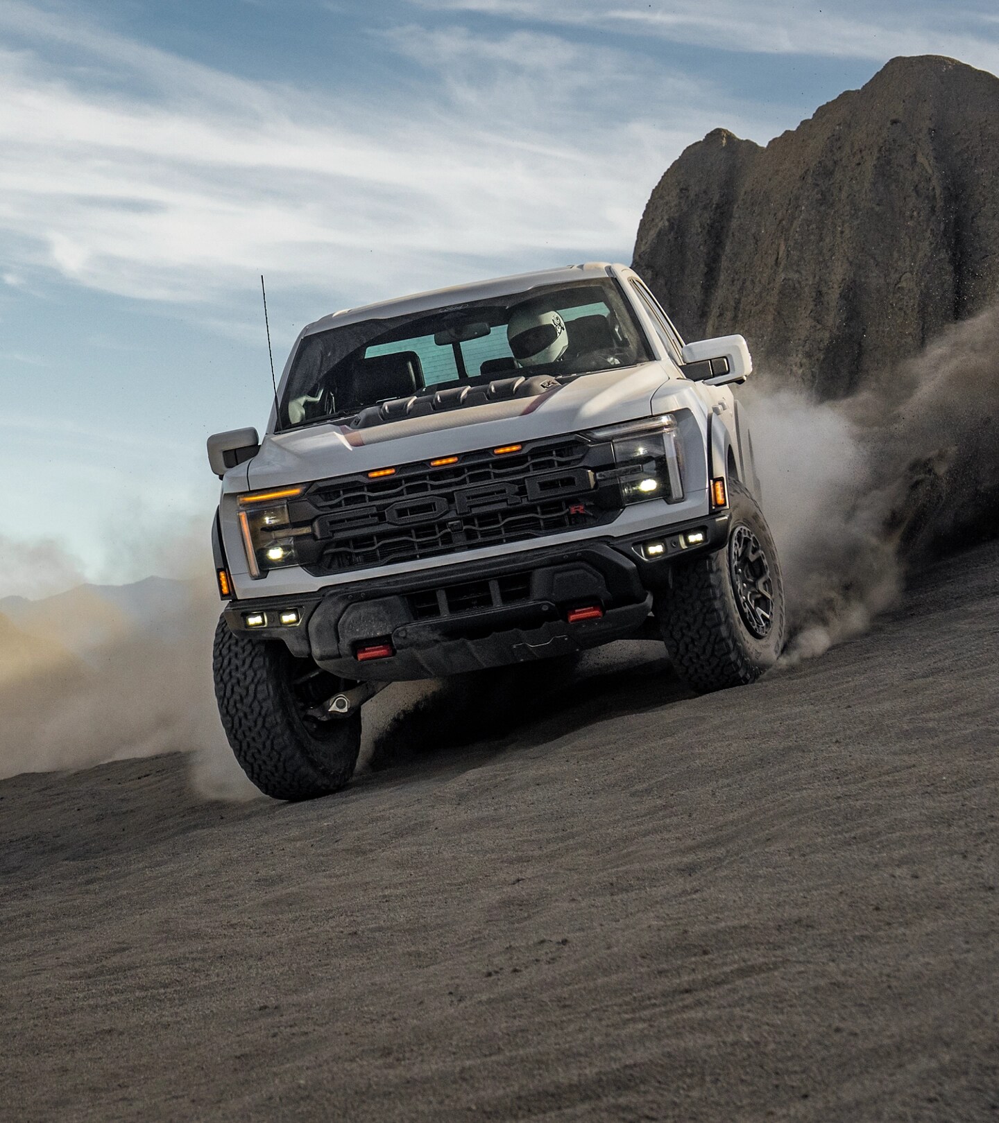 Ford F-150® Raptor® roule en tout-terrain, soulevant la poussière sur une colline rocheuse sous un ciel bleu.