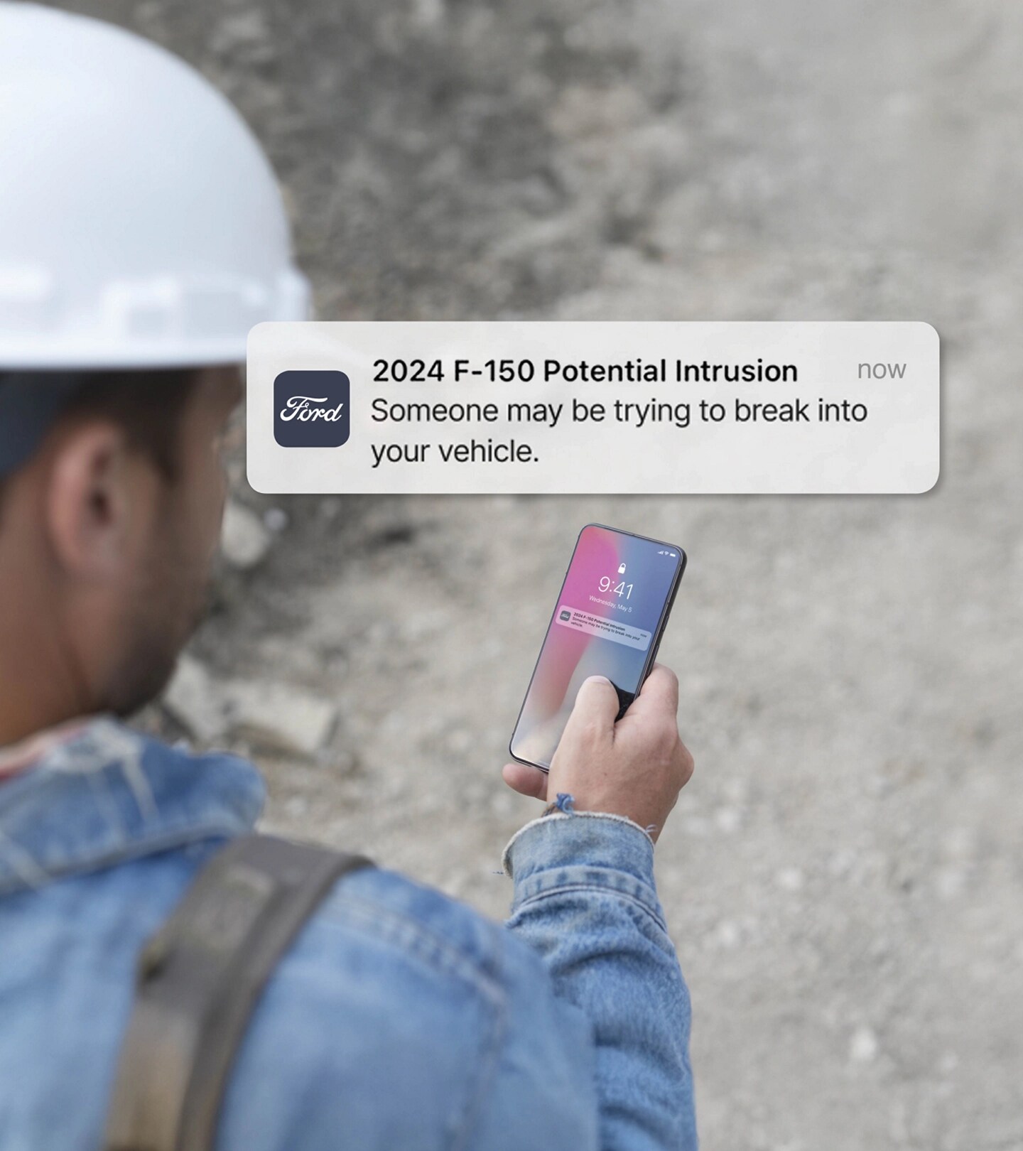 Personne tenant un téléphone intelligent affichant une notification. Superposition du texte qui se lit comme suit : Intrusion potentielle! Quelqu’un peut essayer de pénétrer dans votre véhicule.