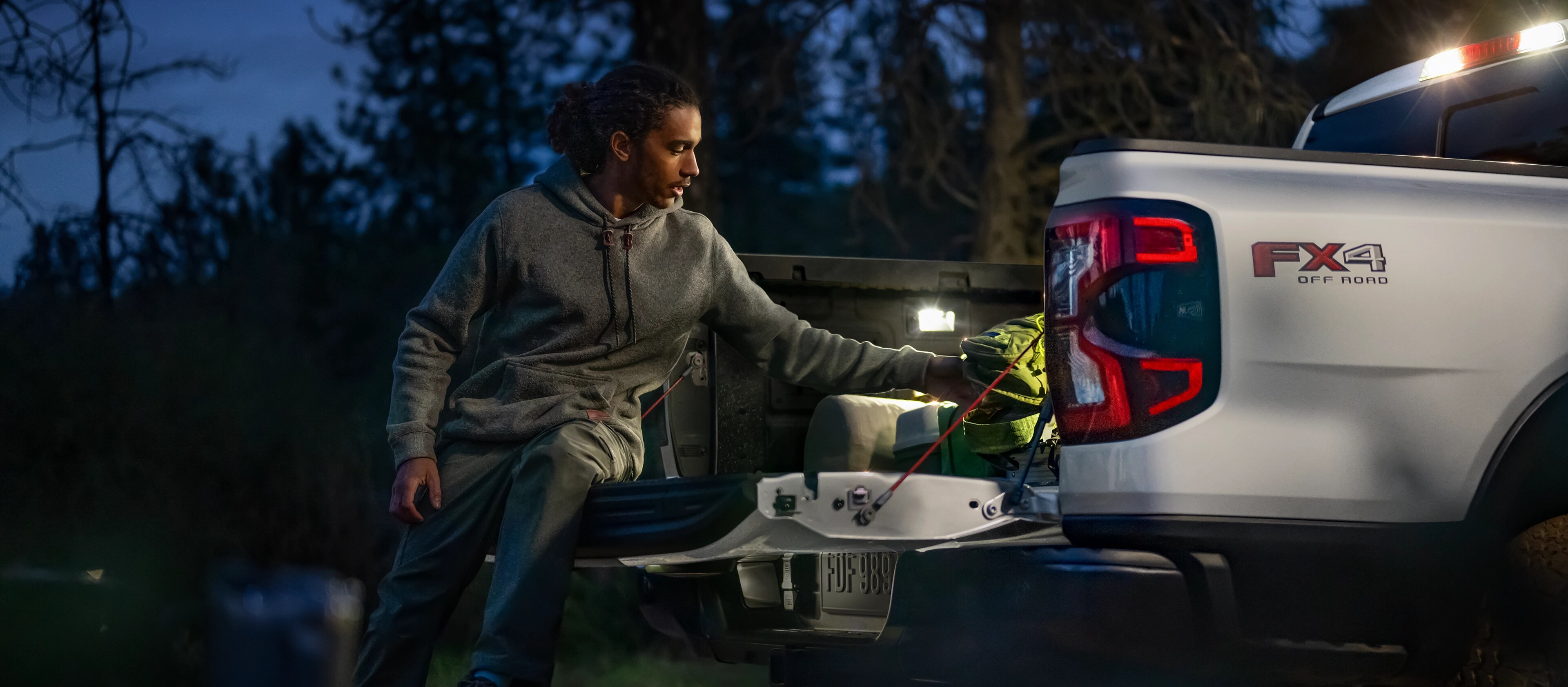 Photo de nuit extérieure présentant un éclairage à DEL de la caisse alors que la personne décharge l’équipement d’un Ford Ranger® 2025