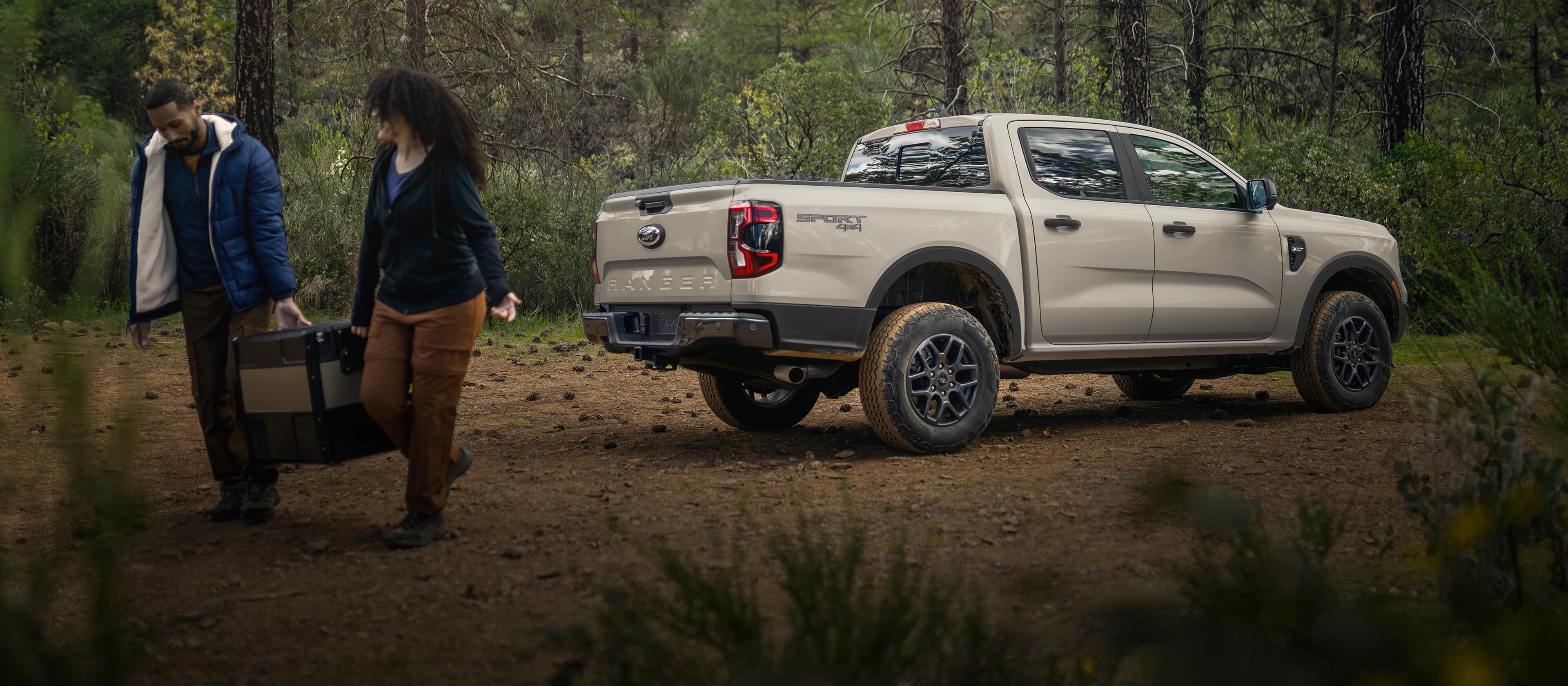 Un Ford Ranger® 2025 stationné dans les bois avec un couple s’éloignant de celui-ci transportant des bagages