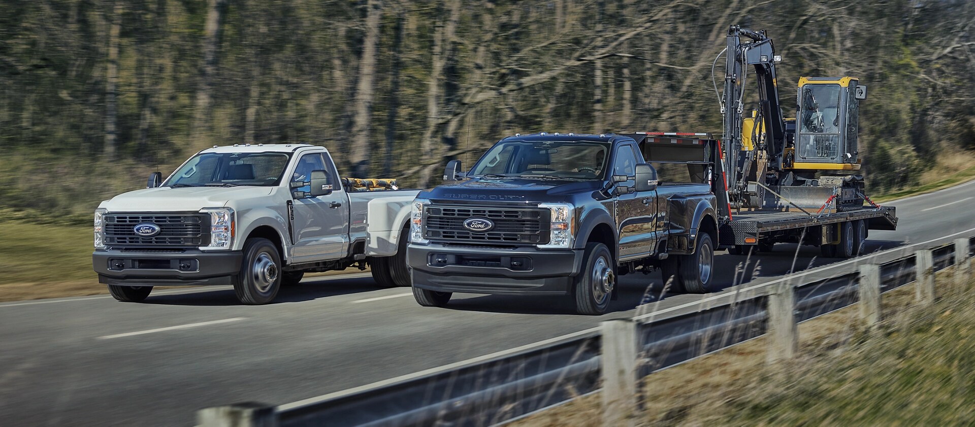 Deux camions Ford Super Duty® 2026, l’un avec de l’équipement dans la caisse et l’autre tirant une grande remorque sur une route pavée