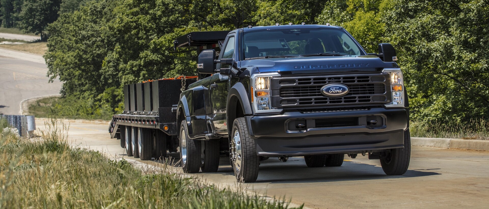 Modèle Ford Super Duty® F-350® Platinum® Plus 2026 en bleu argon tirant une grande remorque à plateau le long d’une colline pavée