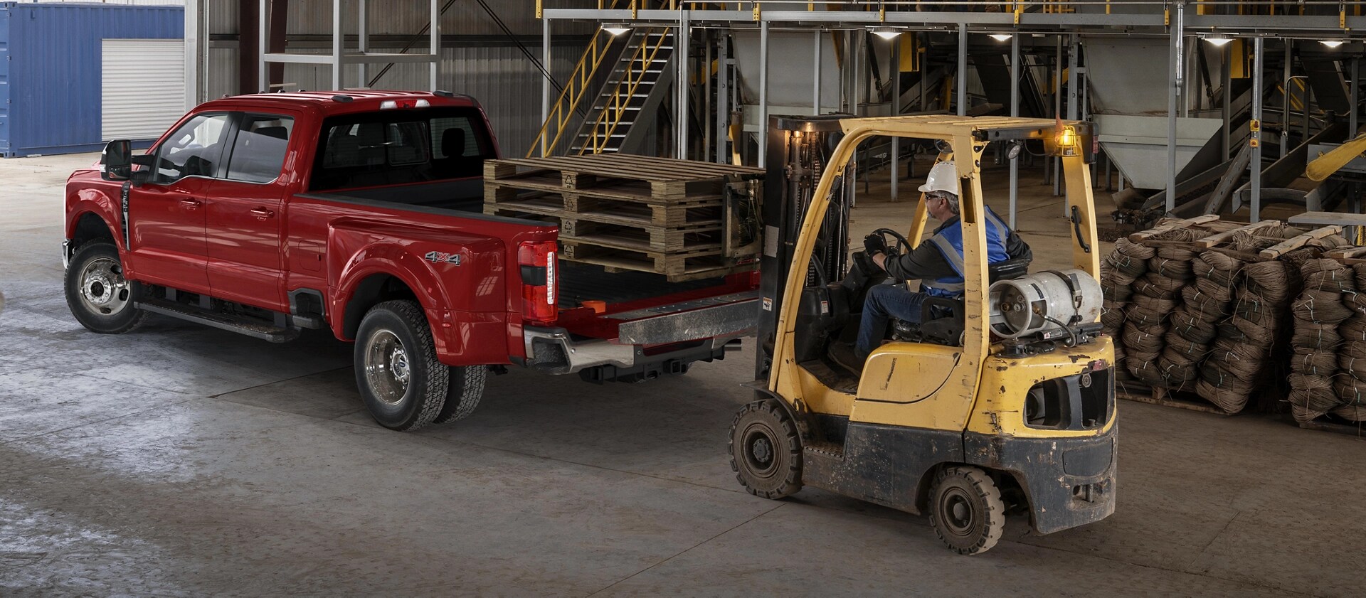 Modèle Ford Super Duty® F-350® Lariat® 2026 avec le hayon ouvert pendant qu’un chariot élévateur charge des palettes en bois dans la caisse du camion