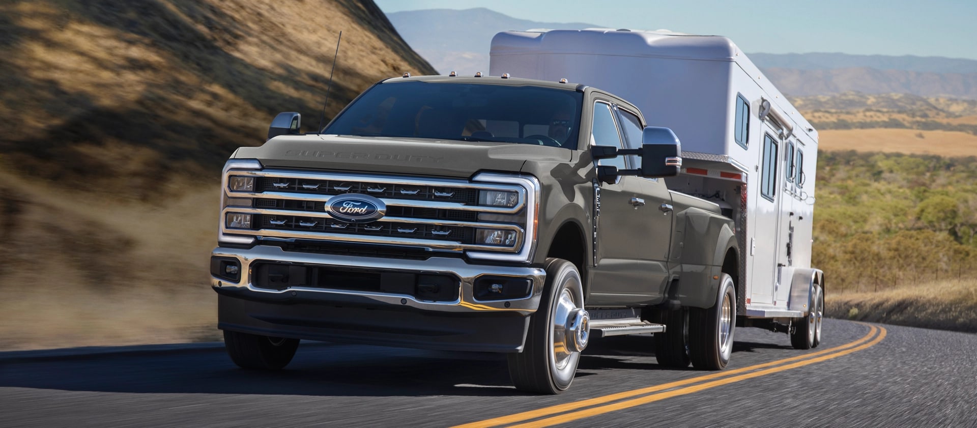 Modèle Ford Super Duty® F-350® Lariat® 2026 en gris marais tirant une remorque sur une route pavée