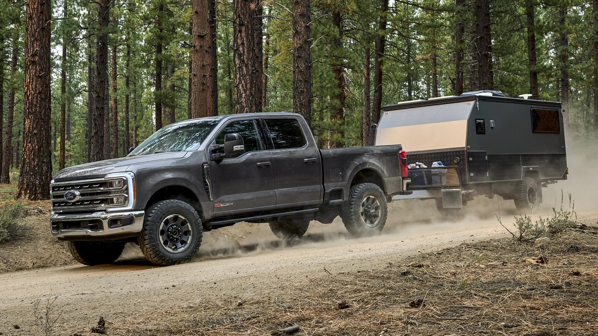 Ford Super Duty® F-250® 2026 avec ensemble tout-terrain Tremor® tirant une remorque sur un chemin de terre dans les bois