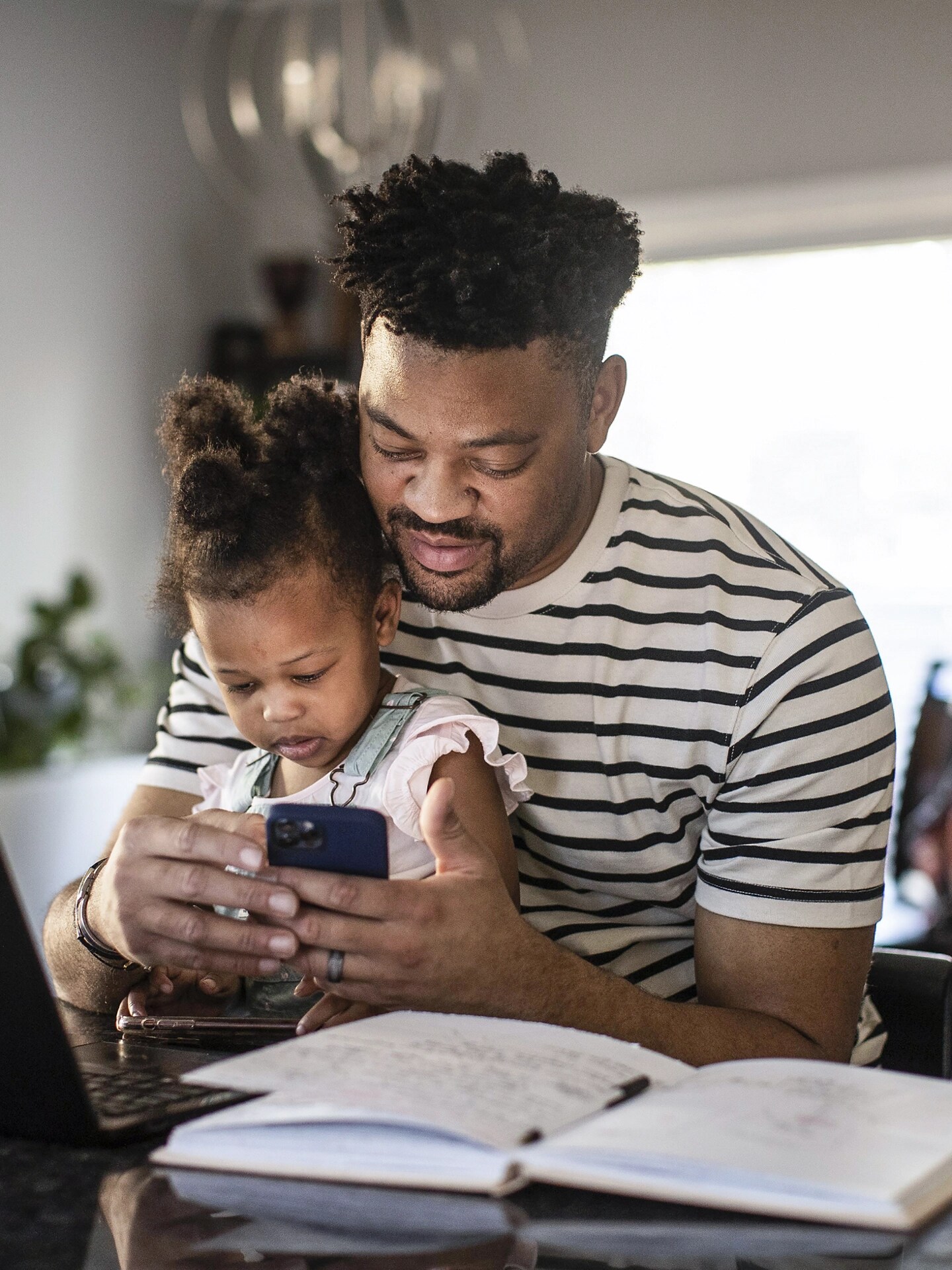 Un homme tient son enfant sur ses genoux tout en interagissant avec l’application FordPass sur son téléphone