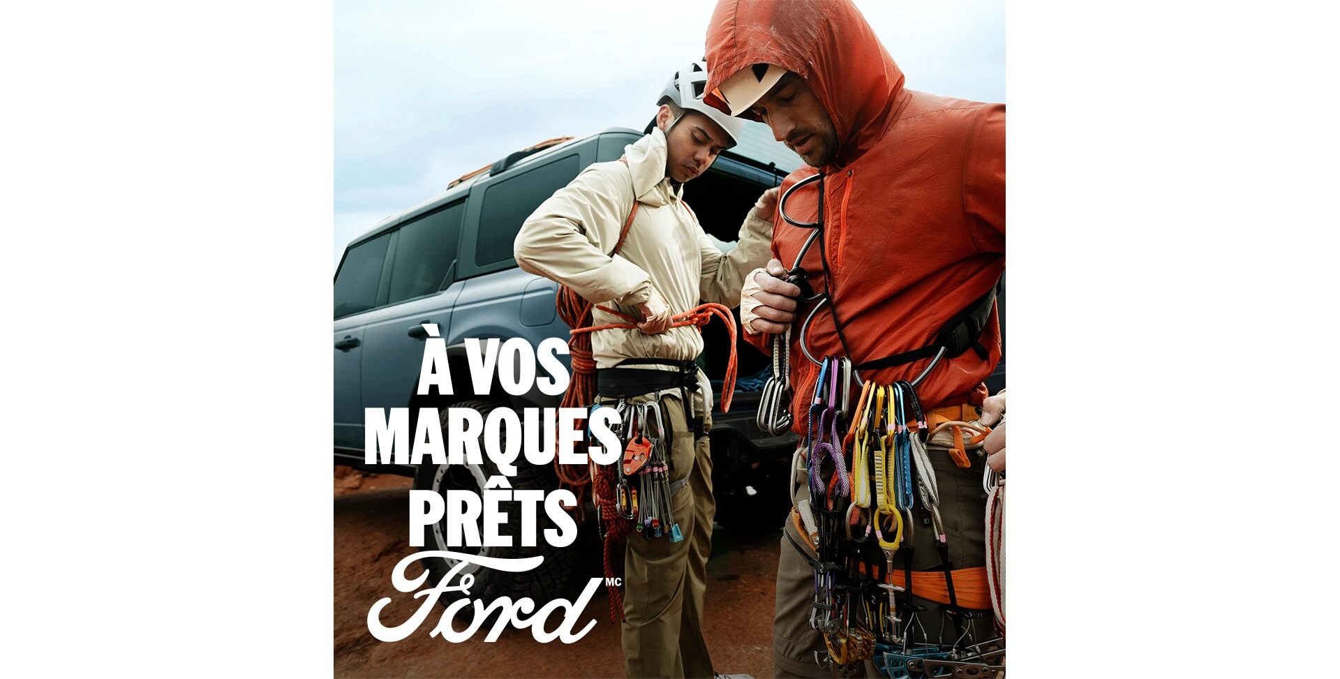 Deux alpinistes masculins se préparent à escalader une paroi rocheuse à côté d'une Ford Bronco gris-bleu. Le texte blanc « À vos marques. Prêts.Ford » apparaît dans le coin inférieur gauche. 