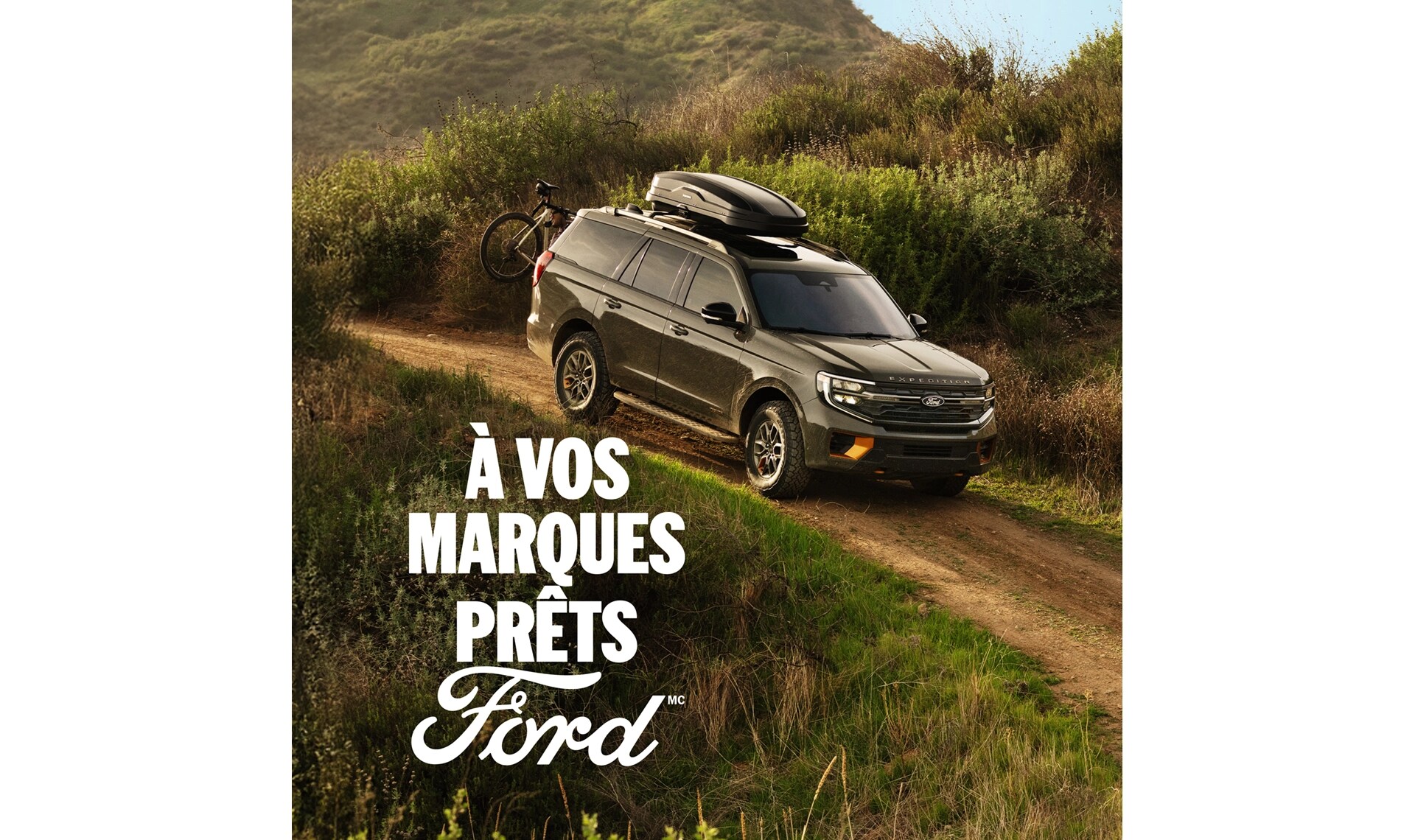 Vue de profil du Ford Expedition 2025 de couleur vert sauvage sur un chemin de terre, avec un vélo de montagne monté à l'arrière. À vos marques, prêts, Ford.