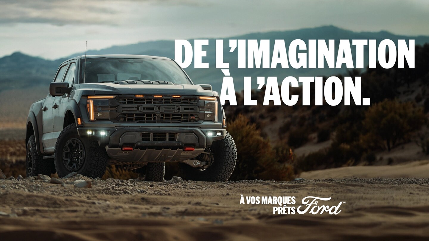 Vue de trois quarts avant d'un Ford F-150 Raptor garé sur un chemin de terre avec des montagnes en arrière-plan. 
