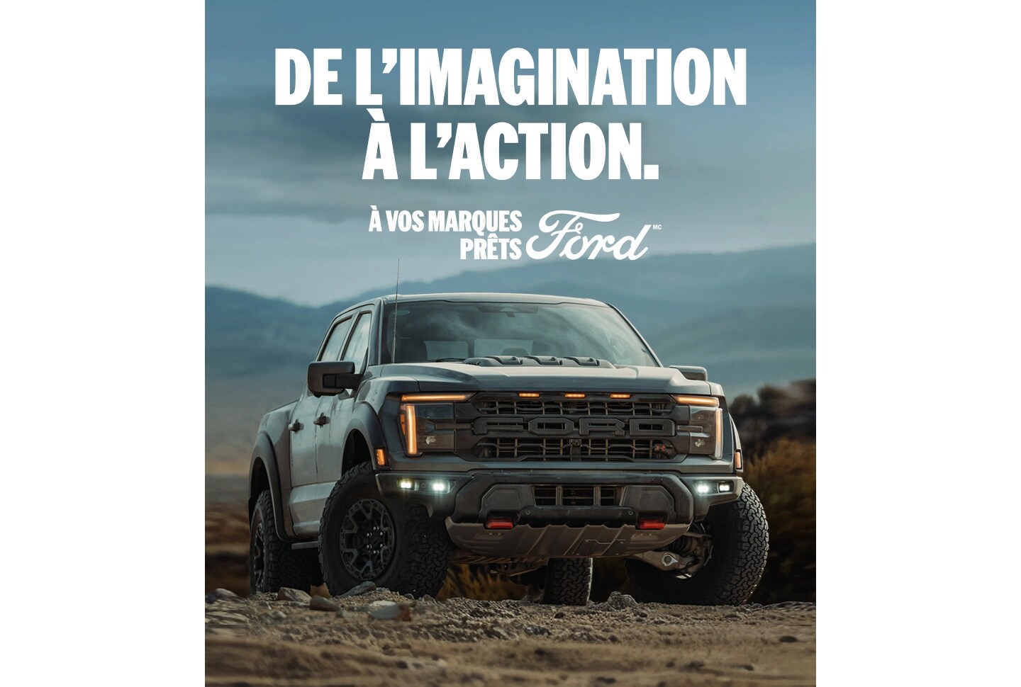 Vue de trois quarts avant d'un Ford F-150 Raptor garé sur un chemin de terre avec des montagnes en arrière-plan. 