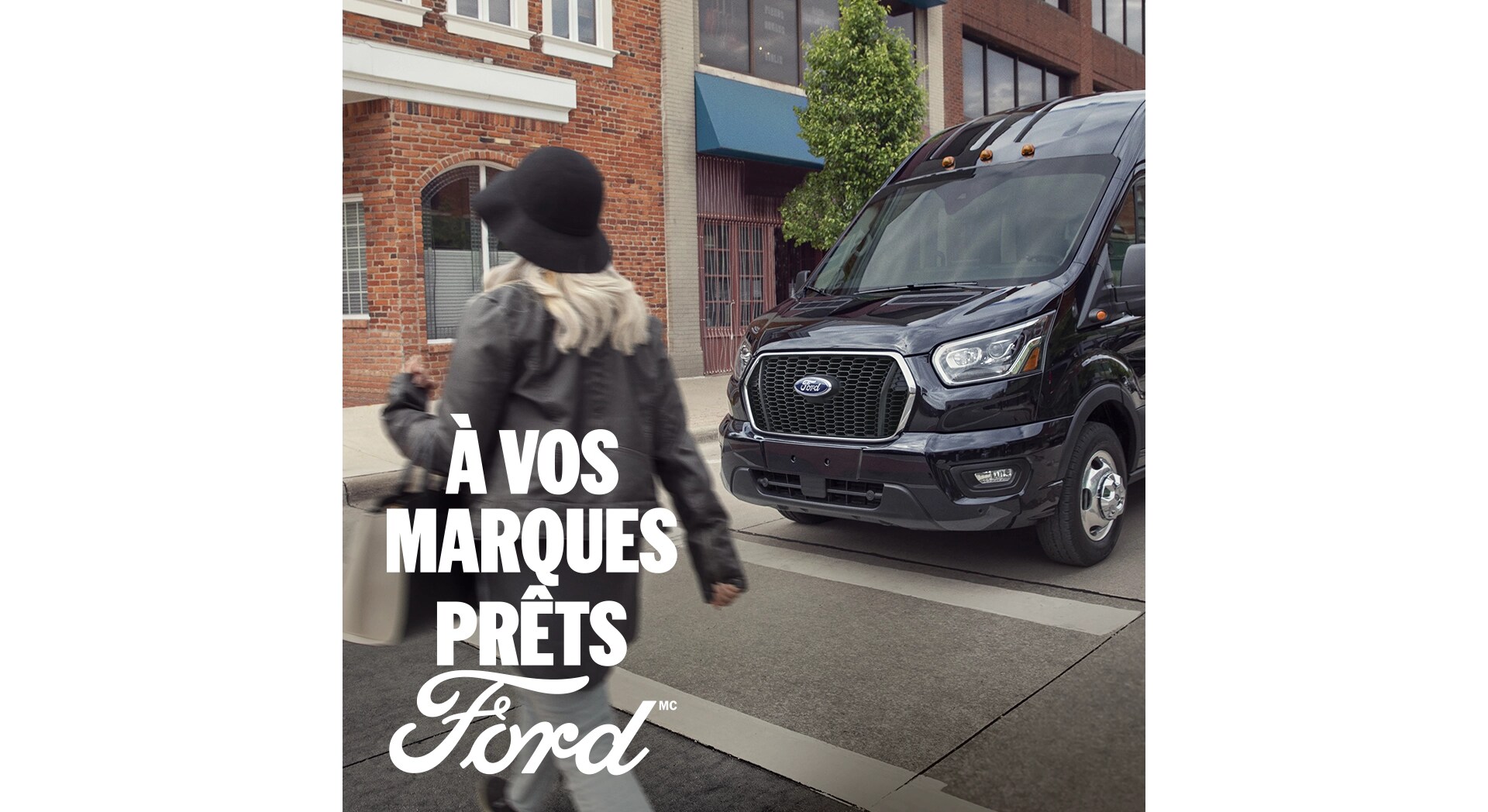 Vue de trois quarts avant d'un Ford Transit 2025 roulant en milieu urbain. À vos marques, prêts, Ford.