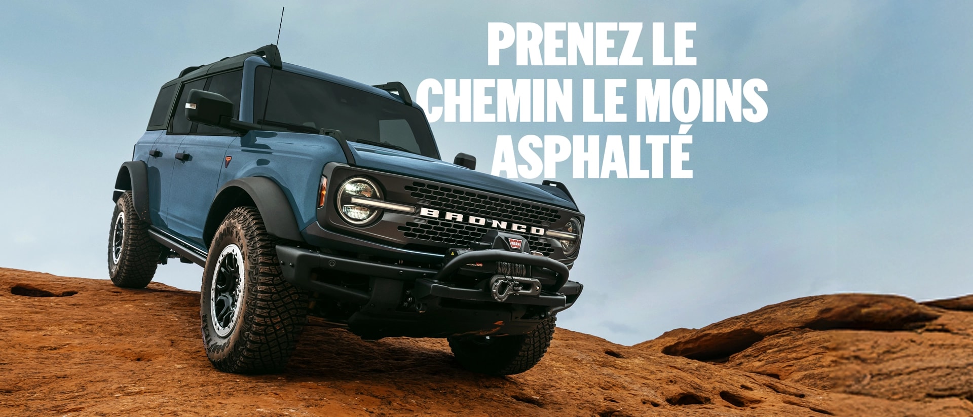 Prenez le chemin le moins asphalté. Vue avant de trois quarts d'un Ford Bronco bleu-gris 2025 descendant un terrain accidenté.