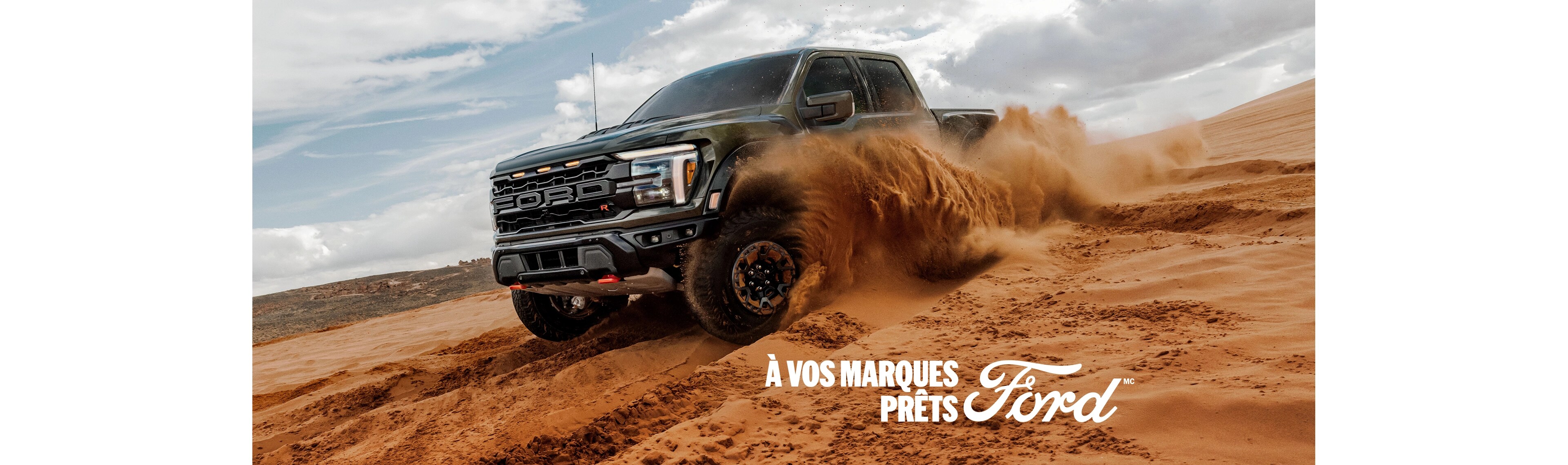 Vue de trois quarts avant d'un Ford F-150 Raptor vert foncé roulant hors route dans du sable profond. Le texte blanc « À vos marques. Prêts. Ford. » apparaît dans le coin inférieur gauche.