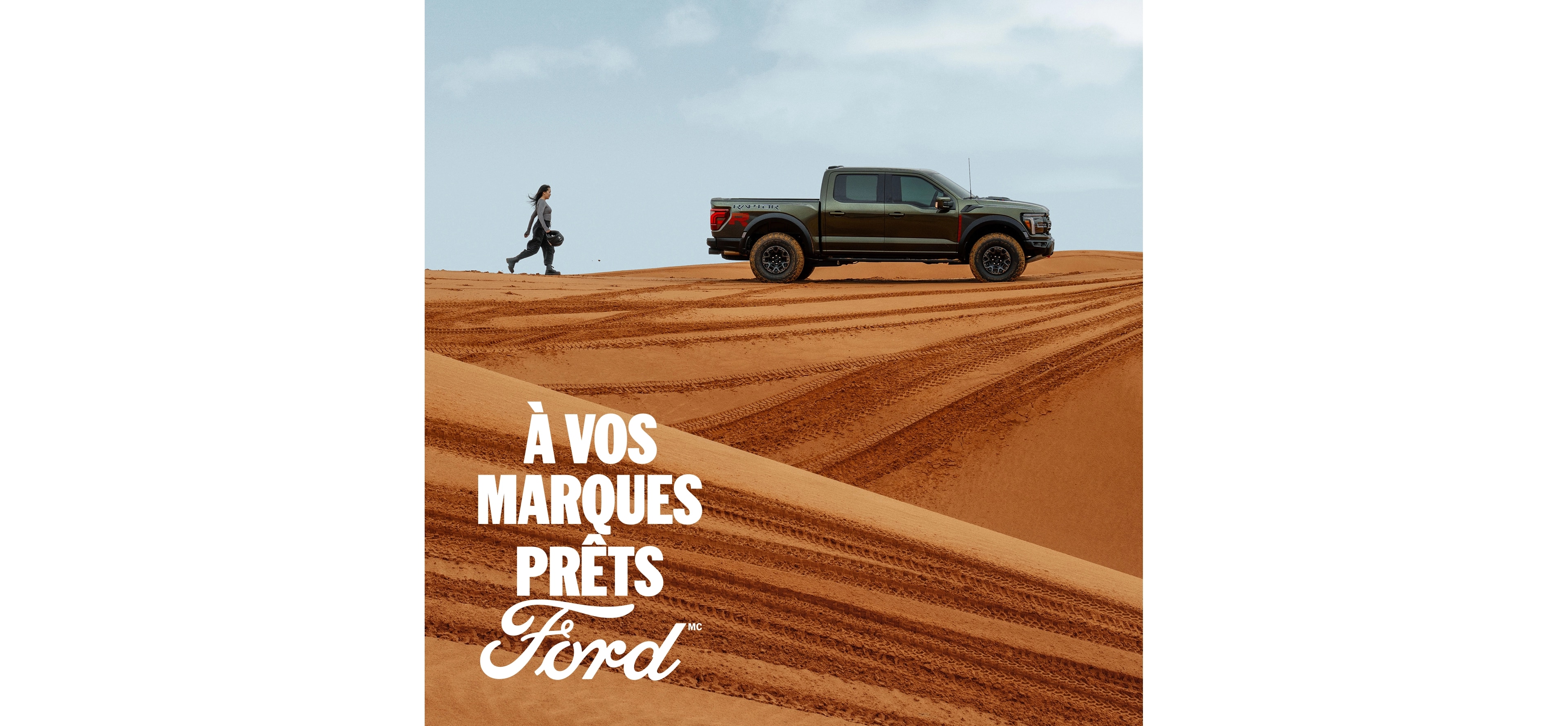 Une femme marche vers l'arrière d'un Ford F-150 Raptor gris, vu de profil, dans un paysage désertique.