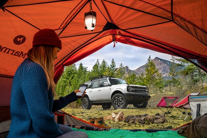 Ford Bronco® Outer Banks™ 4 portières 2023 vu à travers une tente dans laquelle quelqu’un fait du camping