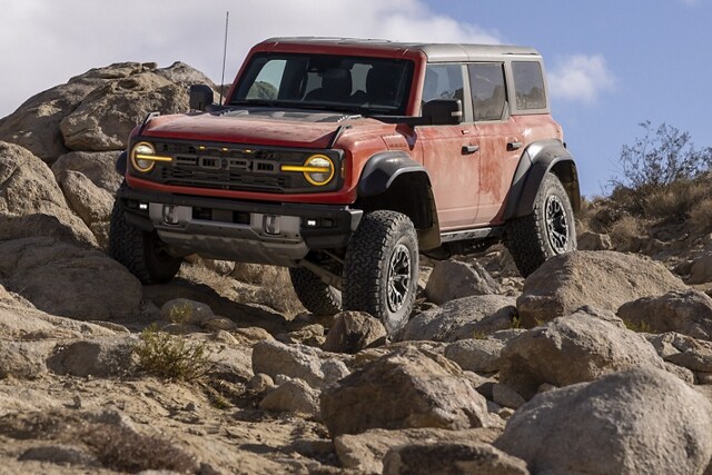 Ford Bronco® Badlands™ 2023 4 portières en rouge piment avec vernis teint métallisé et pare-chocs avant modulaire en option circulant sur des rochers