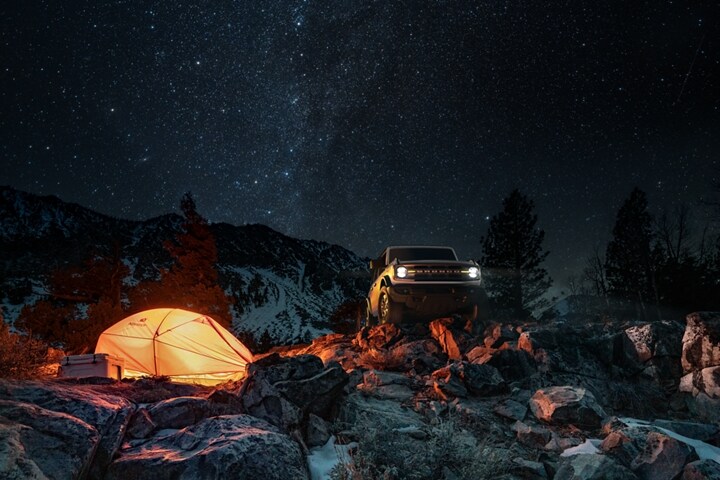 Modèle Ford Bronco® Big Bend™ 2023 2 portières en blanc Oxford stationné près d’un terrain de camping la nuit