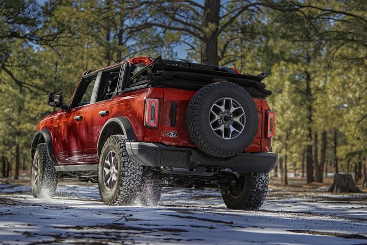 Modèle Ford Bronco® Badlands™ 2023 à 4 portières en rouge piment avec vernis teint métallisé circulant dans une forêt enneigée