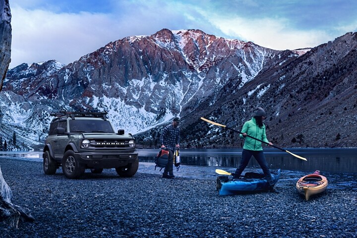 Modèle Ford Bronco® Big Bend™ deux portières 2024 en gris cactus stationné près d’un lac de montagne avec des gens faisant du kayak