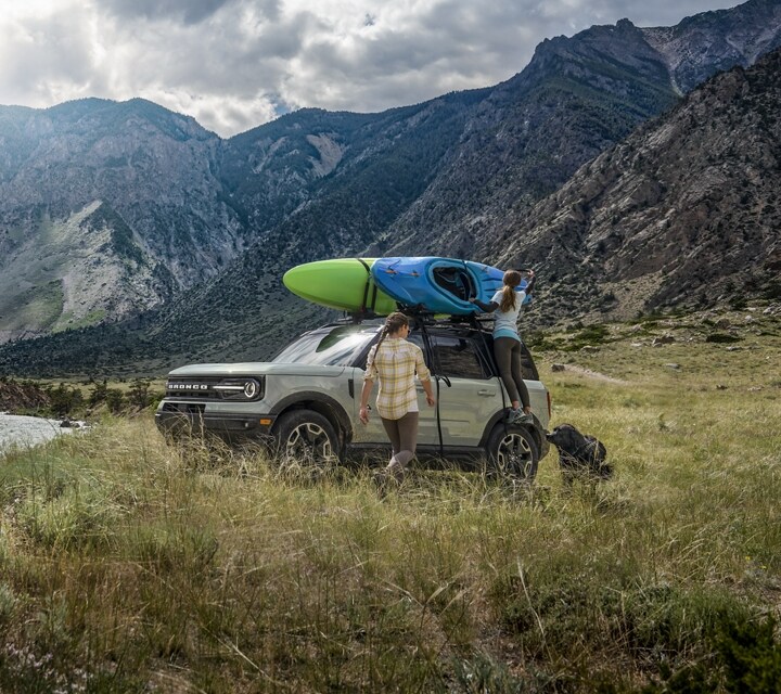 Une personne se tient à l’extérieur d’un VUS Ford Bronco® Sport 2024 stationné près d’un lac avec un kayak sur le toit