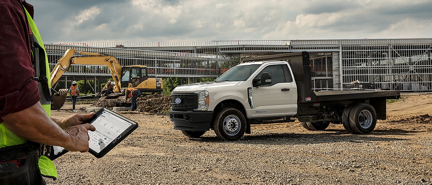 Un Ford Super Duty® F-350 XL 2025 à plateau sur un chantier alors qu’un travailleur utilise une tablette