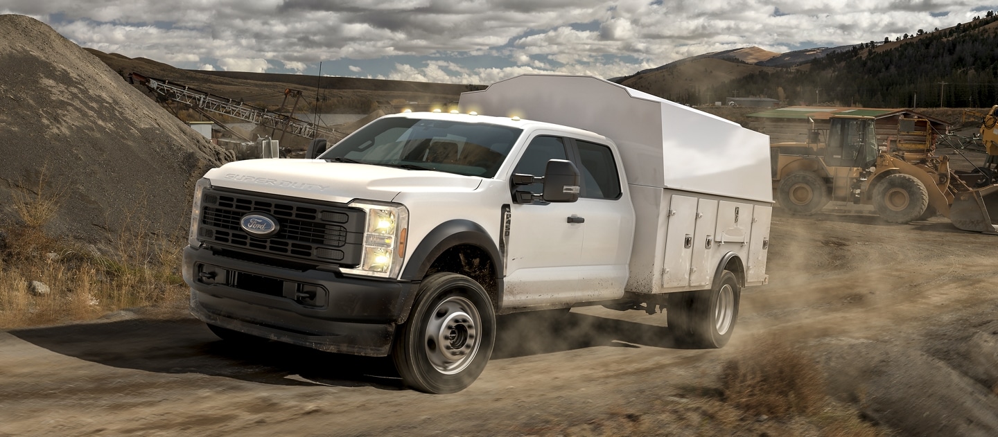 Un Ford Super Duty® F-450® XL 2025 avec une caisse utilitaire remontant un chantier sur un chemin de terre