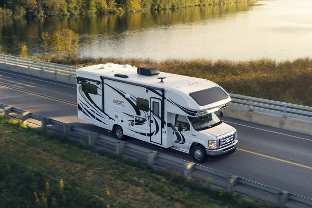 Fourgon tronqué Ford série E 2025 avec autocaravane de classe C circulant près d’un grand plan d’eau