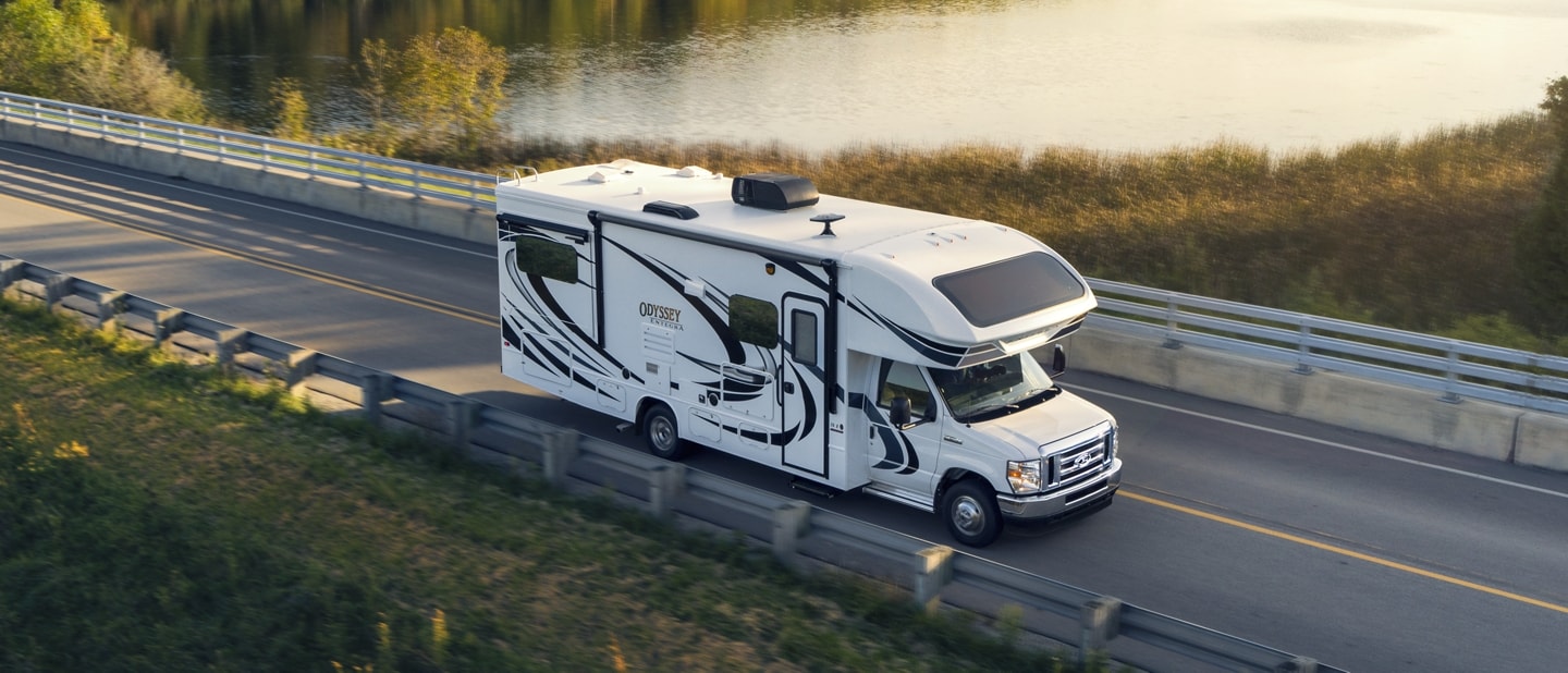 Fourgon tronqué Ford série E 2026 avec autocaravane de classe C circulant près d’un grand plan d’eau