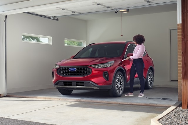 Personne dans un garage chargeant un Ford Escape® hybride rechargeable 2023 au fini vernis métallisé teinté rouge rapide