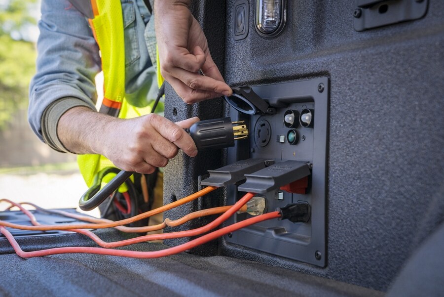 Gros plan d’une personne branchant un cordon dans la prise de courant embarquée professionnelle dans la caisse d’un Ford F-150 2021