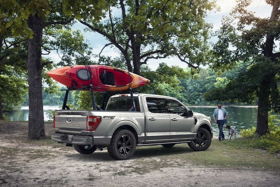 Un Ford F-150® 2023 couleur argent emblématique stationné près d’un lac avec un kayak monté sur un support à kayak faisant partie des accessoires Ford