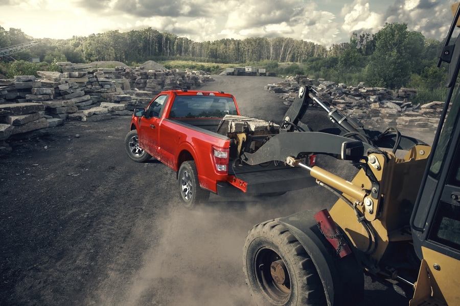 Image d’un tracteur chargeant des matériaux de construction dans la zone du hayon arrière d’un Ford F-150® 2023 sur un chantier