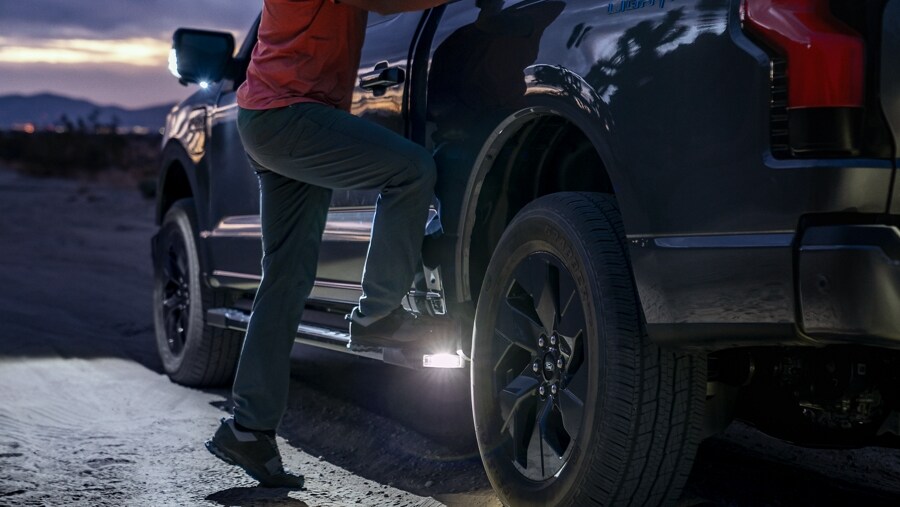 Un homme qui marche sur les marchepieds électriques allongés en option éclairés par une lumière DEL allumée la nuit du Ford F-150® Lightning® 2023