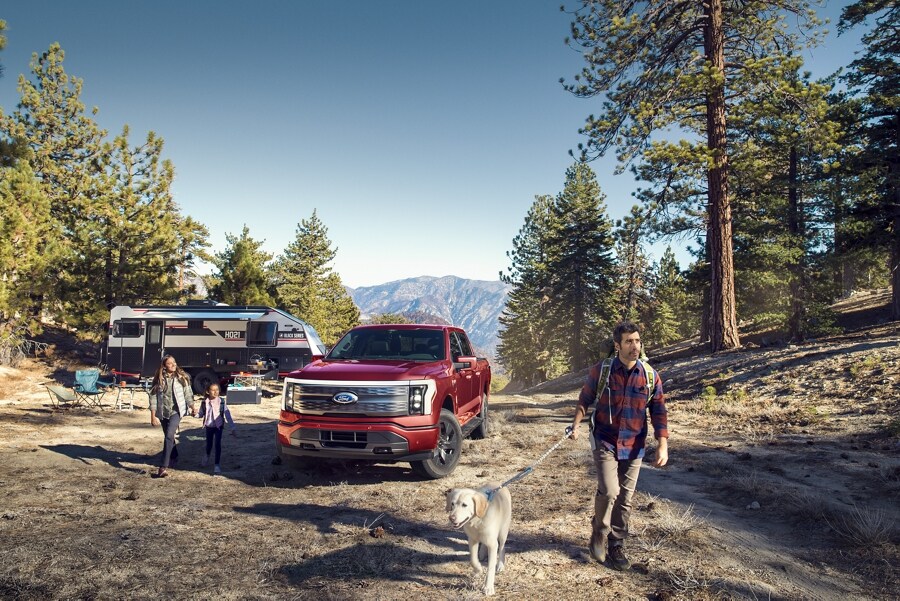Ford F-150® Lightning® 2023 stationné sur un terrain de camping montagneux avec une famille en randonnée avec un chien