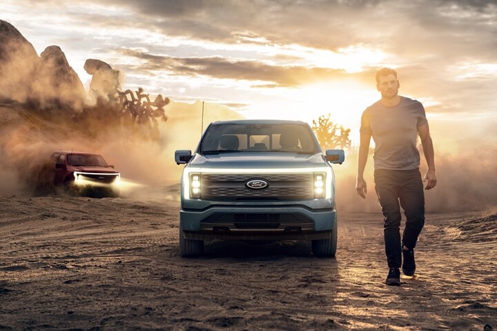 Un homme marche dans le désert au crépuscule, deux camions Ford F-150® Lightning® 2023 conduits derrière lui