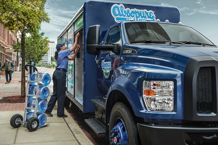 Gros plan sur un travailleur déchargeant de l’eau du Ford F-750 2025 à cabine simple à design personnalisé avec aménagement de camion de boissons dans une rue de la ville