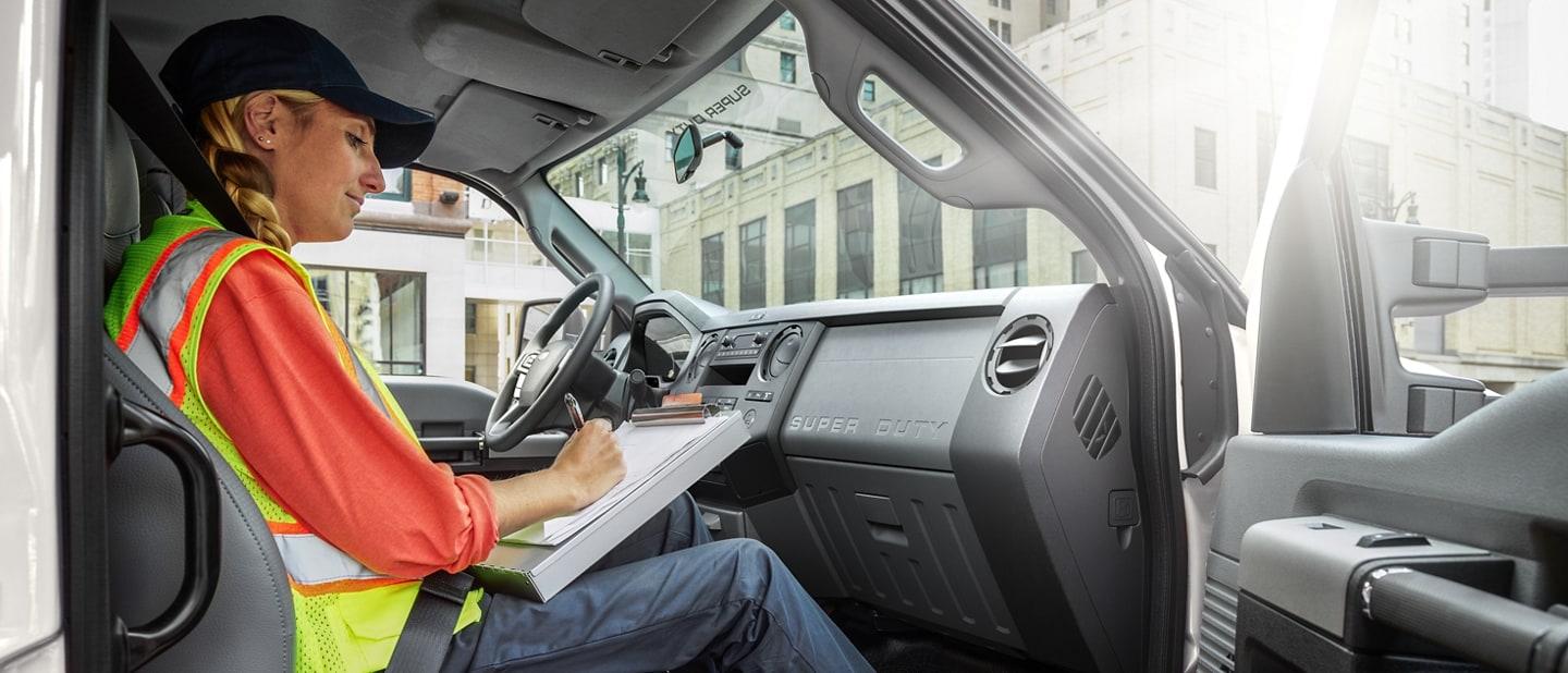 Un travailleur écrivant sur une planchette à pince dans le siège passager du Ford F-750® 2026 à cabine 6 places en blanc Oxford