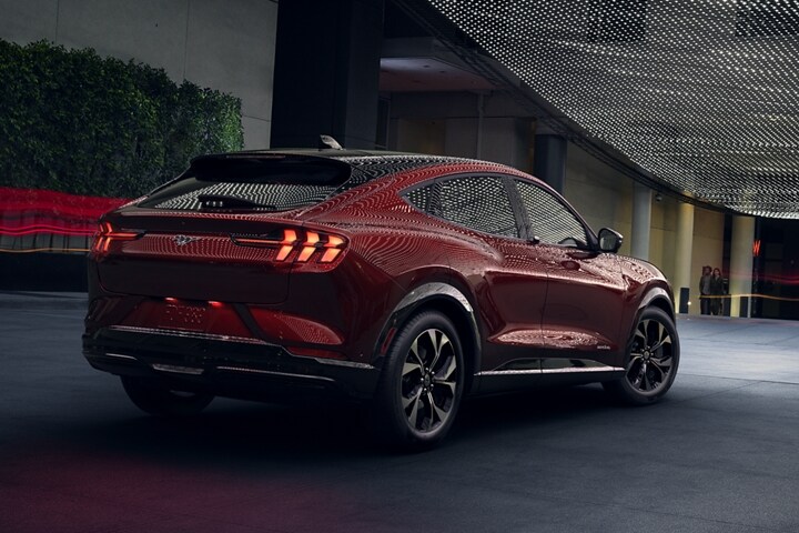 Une femme floue regardant une vue arrière de la Ford Mustang Mach-E® 2023 la nuit sous un éclairage extérieur maussade