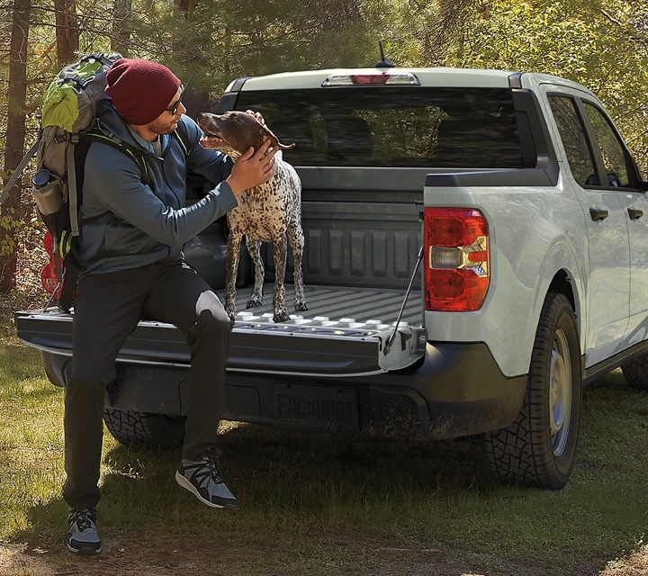 Un camion Ford Maverick® 2024 stationné dans un endroit pittoresque avec une personne et un chien dans la caisse du camion