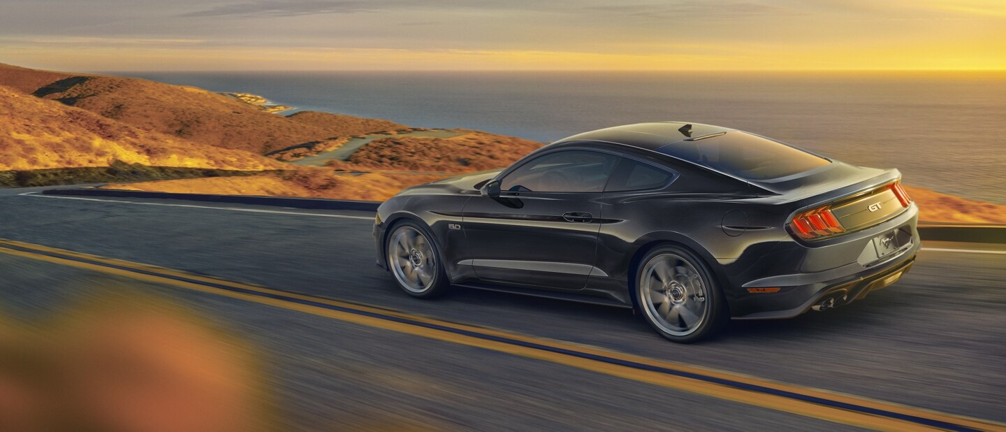 Une Ford Mustang® coupé 2023 en noir ombre circulant sur une autoroute au bord de l’océan