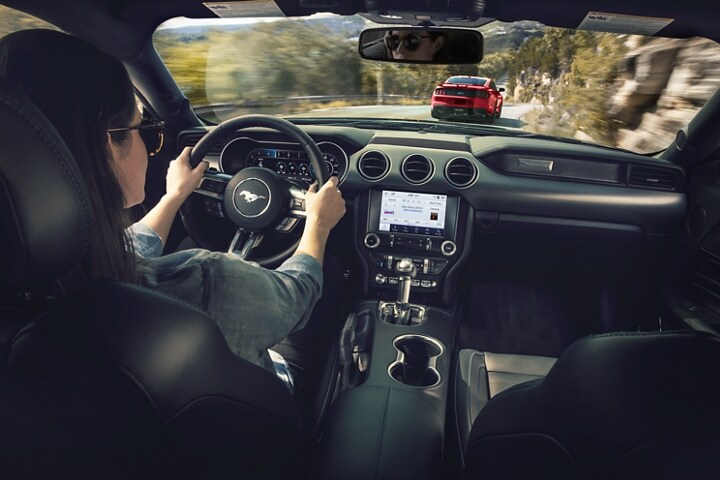 Une personne derrière le volant d’une Ford Mustang® coupé 2023 roulant sur une route montagneuse