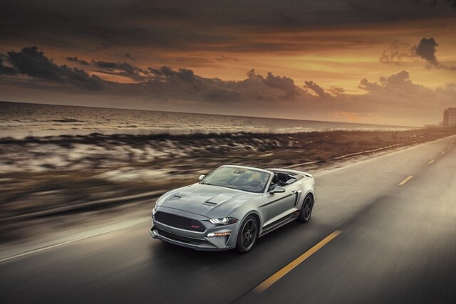 Ford Mustang® 2023 décapotable avec ensemble California Special, le toit baissé circulant sur une autoroute au bord de l’océan