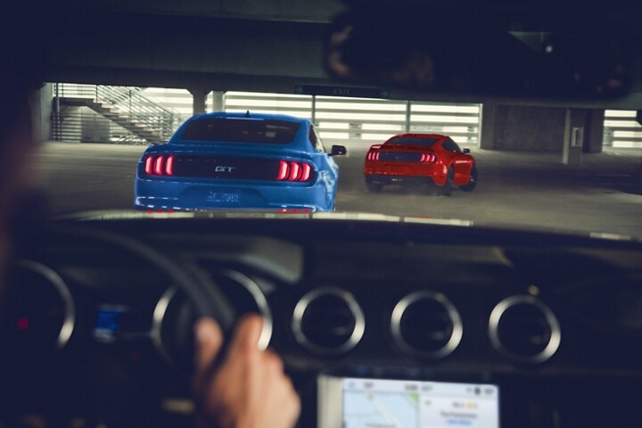 Vue à travers le pare-brise d'une Ford Mustang®  coupé 2023 conduisant dans un stationnement à la suite de deux autres modèles de Mustang