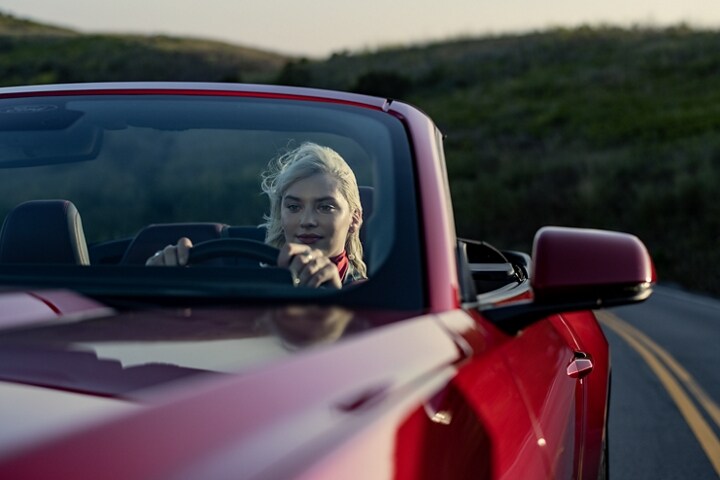 Personne conduisant un modèle Ford Mustang® décapotable 2024 en rouge rapide avec teint métallisé (peinture à coût supplémentaire) sur une autoroute