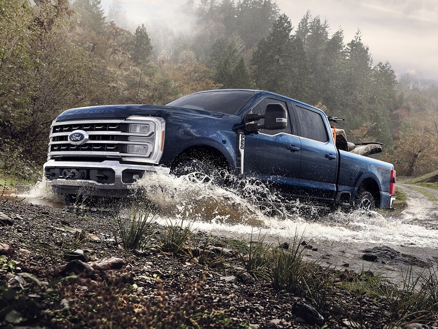 Modèle Ford Super Duty® F-250® TREMOR™ 2025 en bleu antimatière circulant dans une rivière peu profonde
