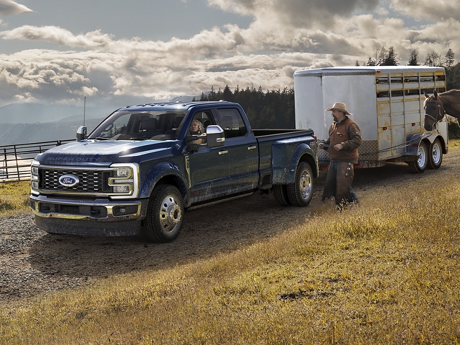 Un homme faisant marcher un cheval près d’un Ford Super Duty® F-450® King Ranch® 2025 à RAJ en bleu antimatière fixé à une remorque à cheval