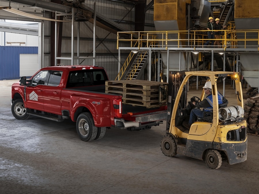 Chariot élévateur à fourche chargeant une palette de foin dans la caisse d’un modèle Ford Super Duty® F-350® LARIAT® à RAJ 2025 en rouge rapide