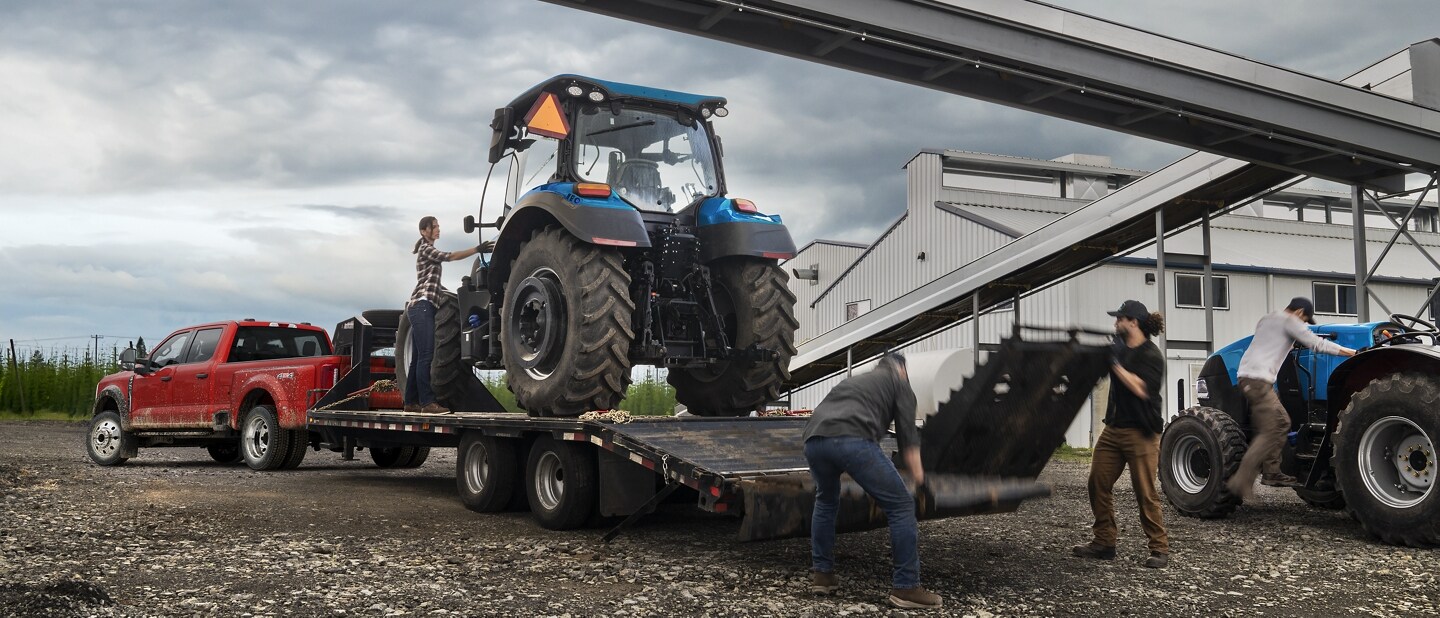 Trois personnes chargeant un tracteur sur une remorque à plateau attachée à un modèle Ford Super Duty® F-450® XL à RAJ 2025 en rouge rapide